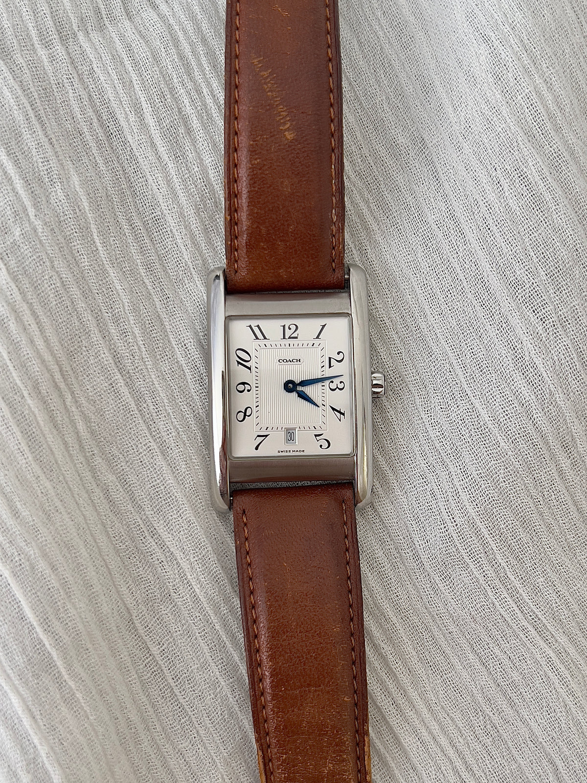 Close-up of the silver dial with black Arabic numerals and blued hands on a Coach watch.