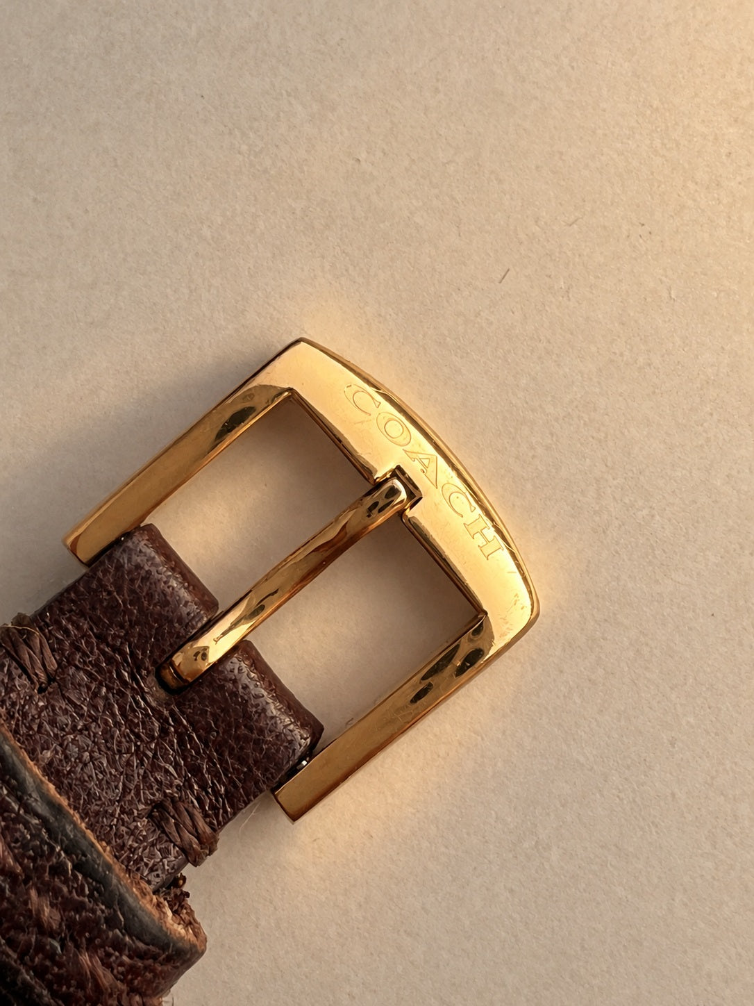 Coach signed gold tone pin buckle on a worn brown leather watch strap