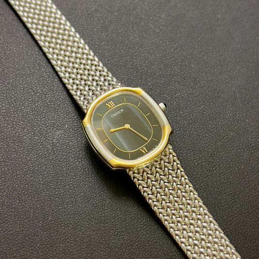 Credor women’s watch with a black dancing dial, gold-tone case accents, and mesh bracelet.