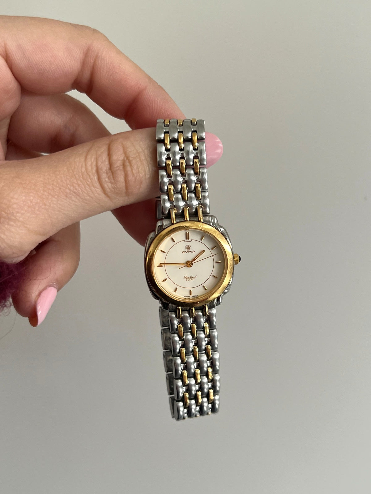 Front view of the Cyma Sealord with round gold tone bezel and silver bracelet threaded with three gold tone rows.