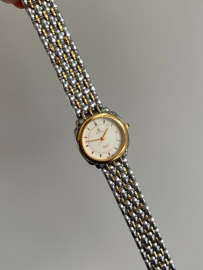 Cyma Sealord round women’s watch with its two tone bracelet extended at an angle.