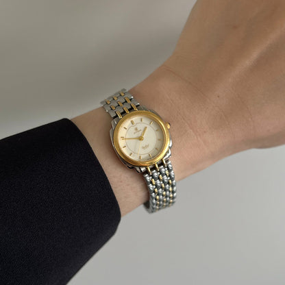 Cyma Sealord cream dial two tone women’s watch worn on a wrist beside a black sleeve.