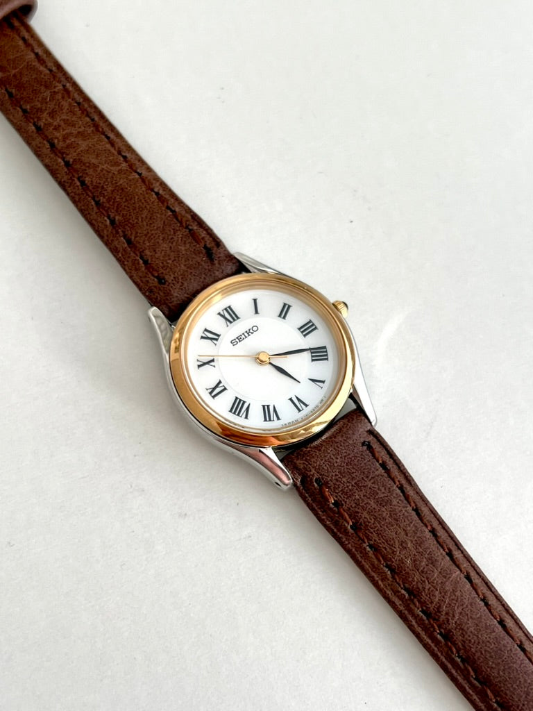 Close-up of the Seiko Exceline white Roman numeral dial, black hands, gold tone bezel and brown leather strap