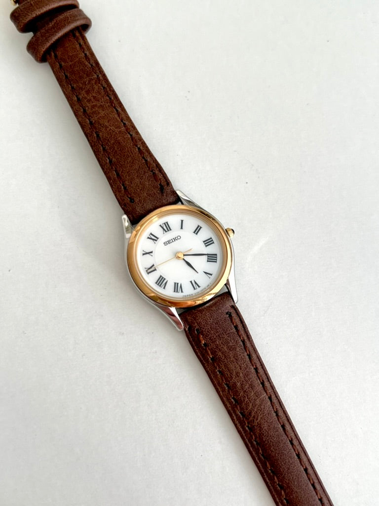 Seiko Exceline round two tone watch with white Roman dial and stitched brown leather strap on a pale background