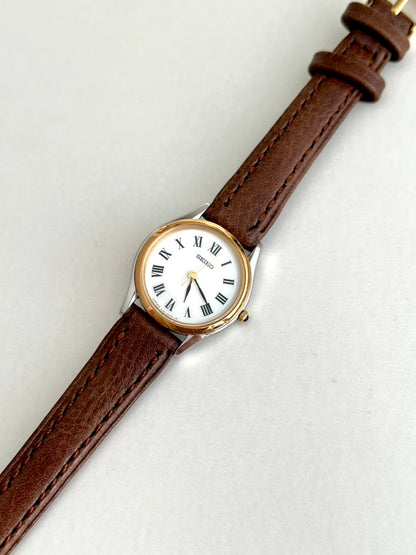 Angled front view of the Seiko Exceline white Roman dial with black leaf shaped hands and polished two tone case