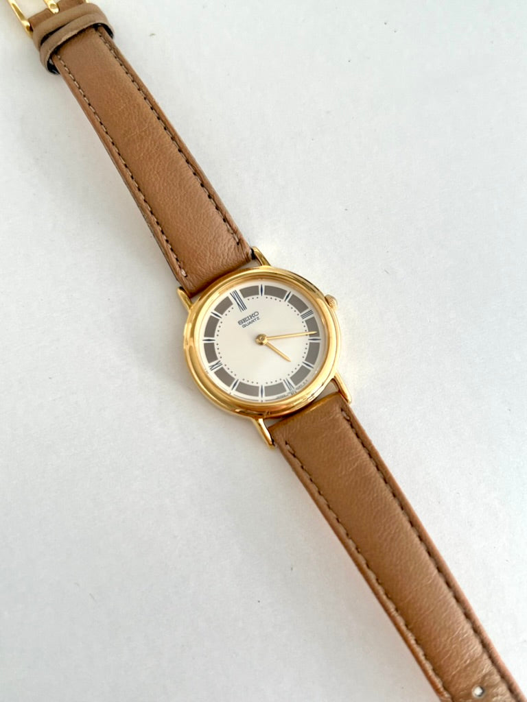 Seiko round gold tone watch on a stitched tan leather strap, photographed diagonally