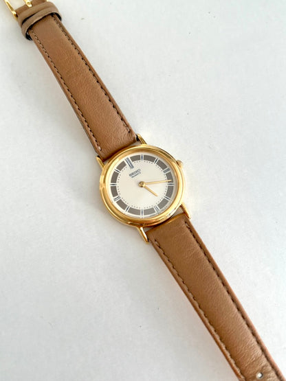 Seiko round gold tone watch on a stitched tan leather strap, photographed diagonally