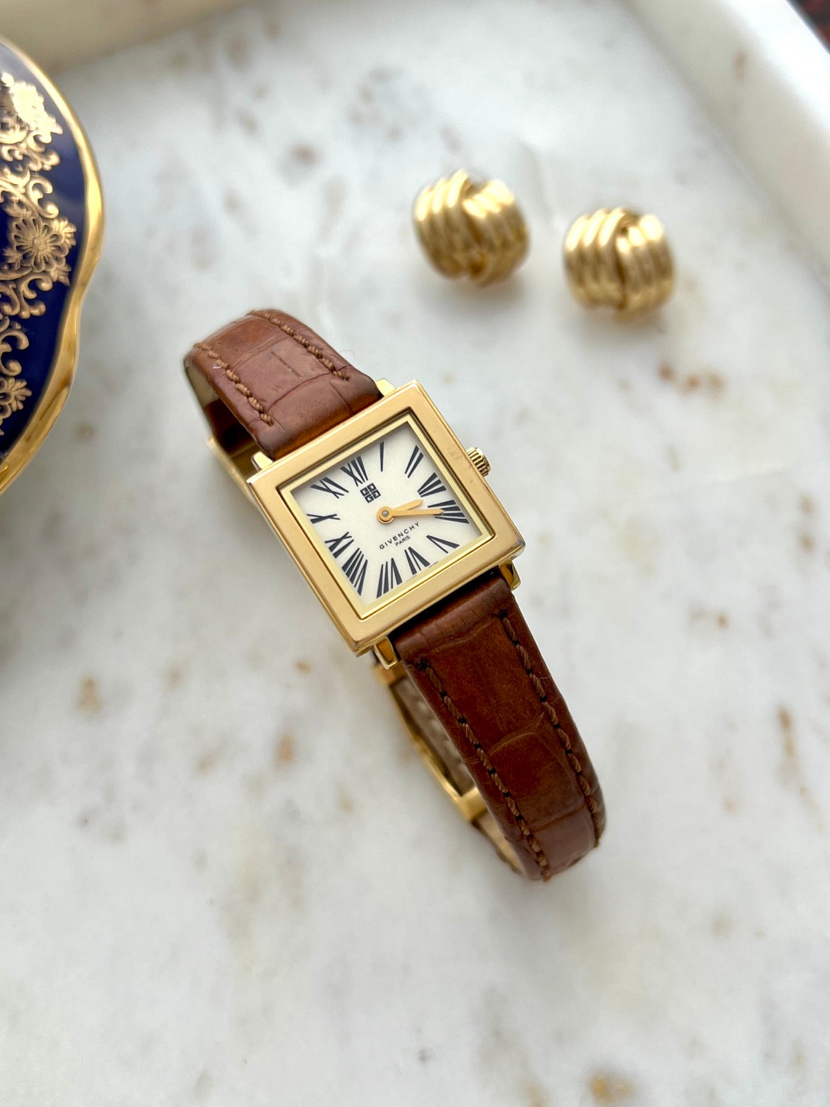 Givenchy rectangular gold tone watch with brown patterned leather strap in a marble still life