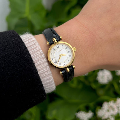 Gucci 2040L Roman dial women’s watch worn on wrist with gold tone case and black leather strap