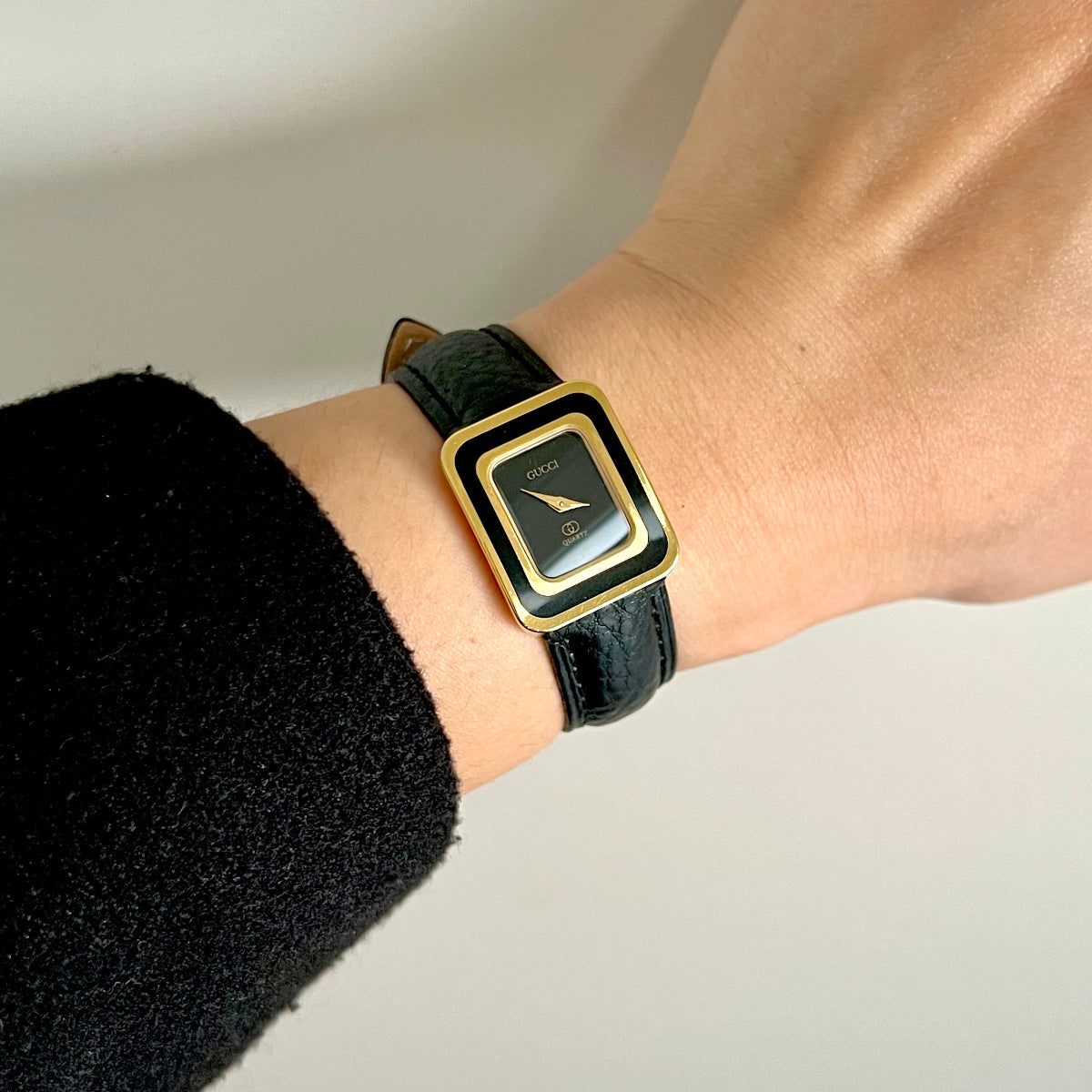 Vintage Gucci women’s watch with black dial, gold tone rectangular case and black leather strap shown on wrist