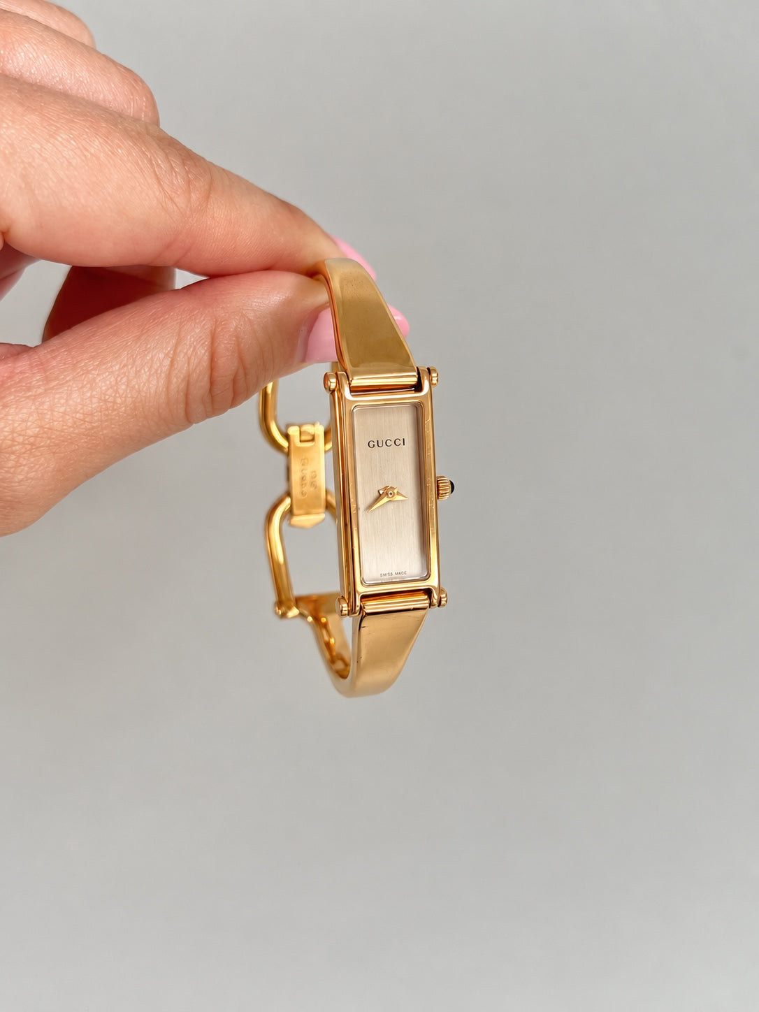 Front view of the Gucci women’s rose gold tone bangle watch with a brushed champagne dial and sculptural hands, held against a neutral background