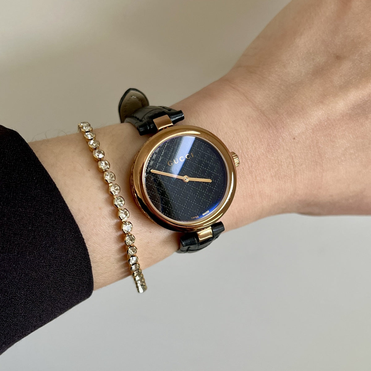 Gucci Diamantissima rose gold tone women’s watch with a dark patterned dial and black leather strap pictured on a 15cm wrist.