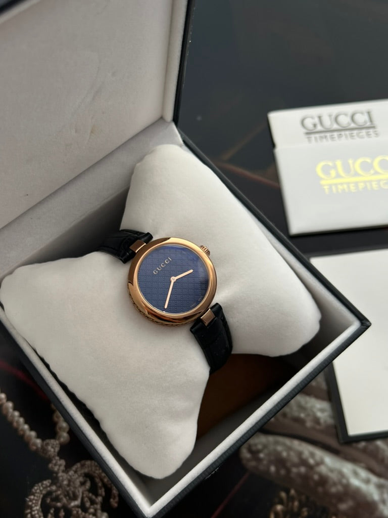 Closer view of the Gucci Diamantissima patterned dark dial, polished rose gold tone bezel and black leather strap.