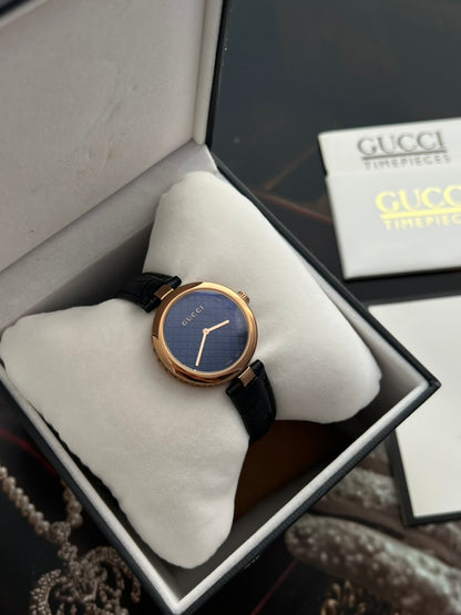Closer view of the Gucci Diamantissima patterned dark dial, polished rose gold tone bezel and black leather strap.