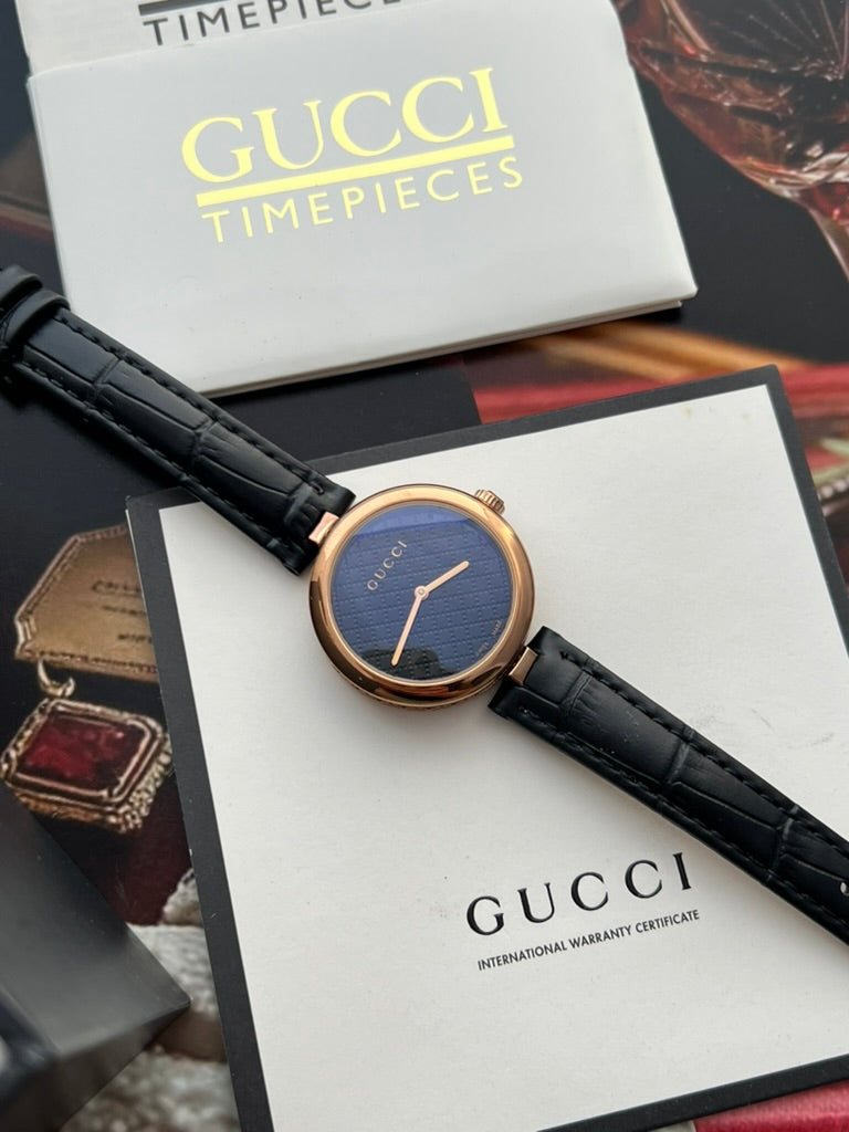 Gucci Diamantissima watch resting on photographed Gucci paperwork, with blue reflections over the dark Diamante patterned dial.