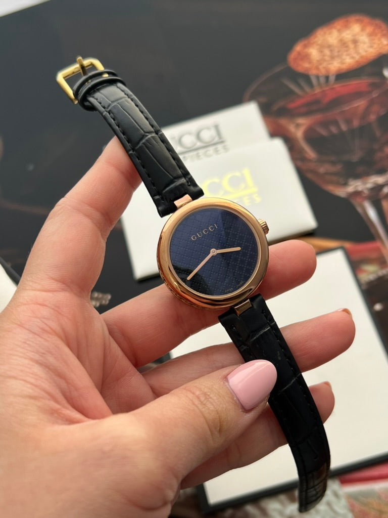 Full view of the Gucci Diamantissima women’s watch with its black embossed leather strap and gold tone pin buckle.
