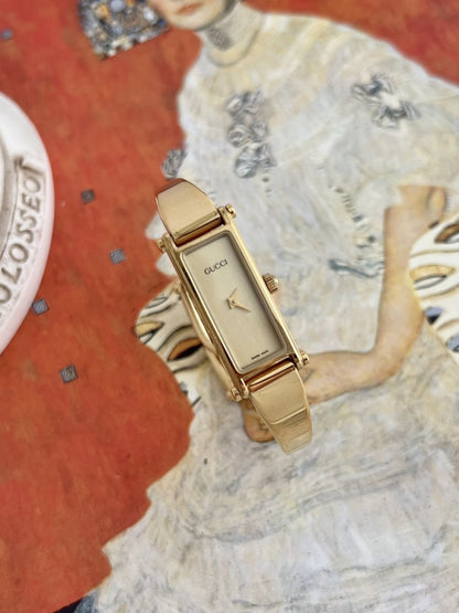Right angled view of the Gucci women’s rectangular champagne dial and curved gold tone bangle