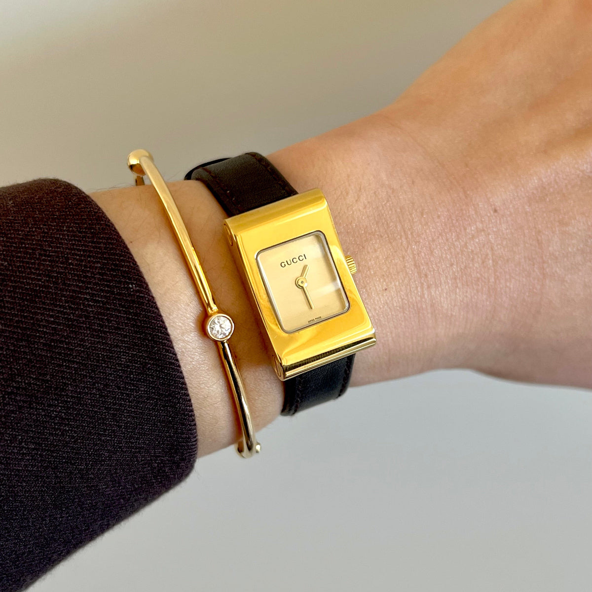 Gucci women's watch with gold rectangular case, champagne dial and black leather strap worn on wrist
