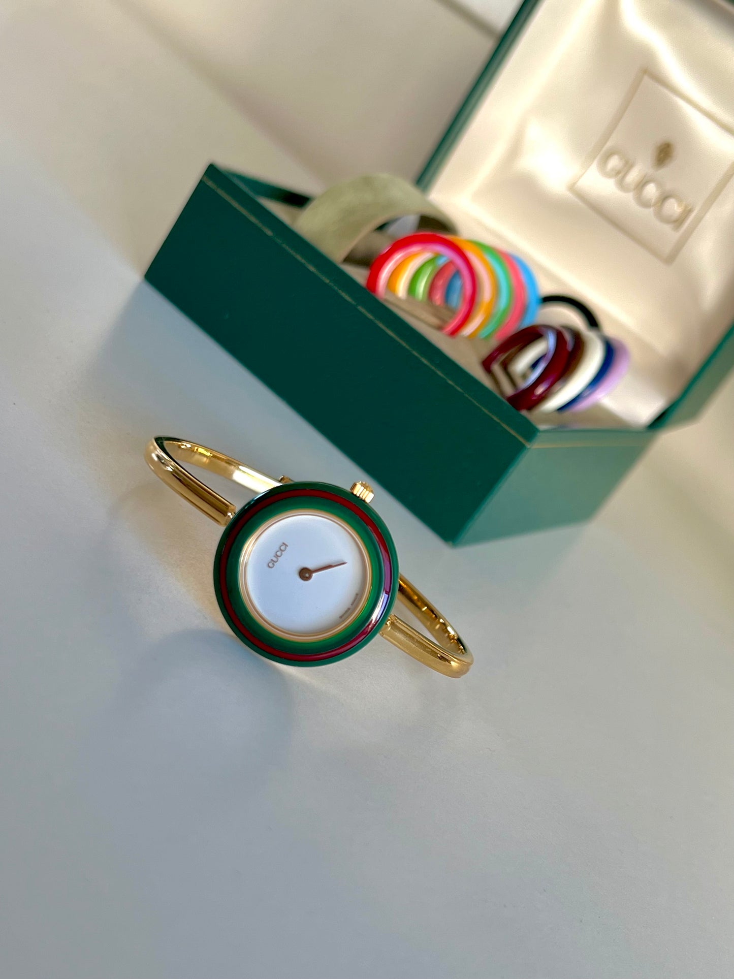 Gucci interchangeable bezel watch with signature green and red bezel on gold tone bangle bracelet