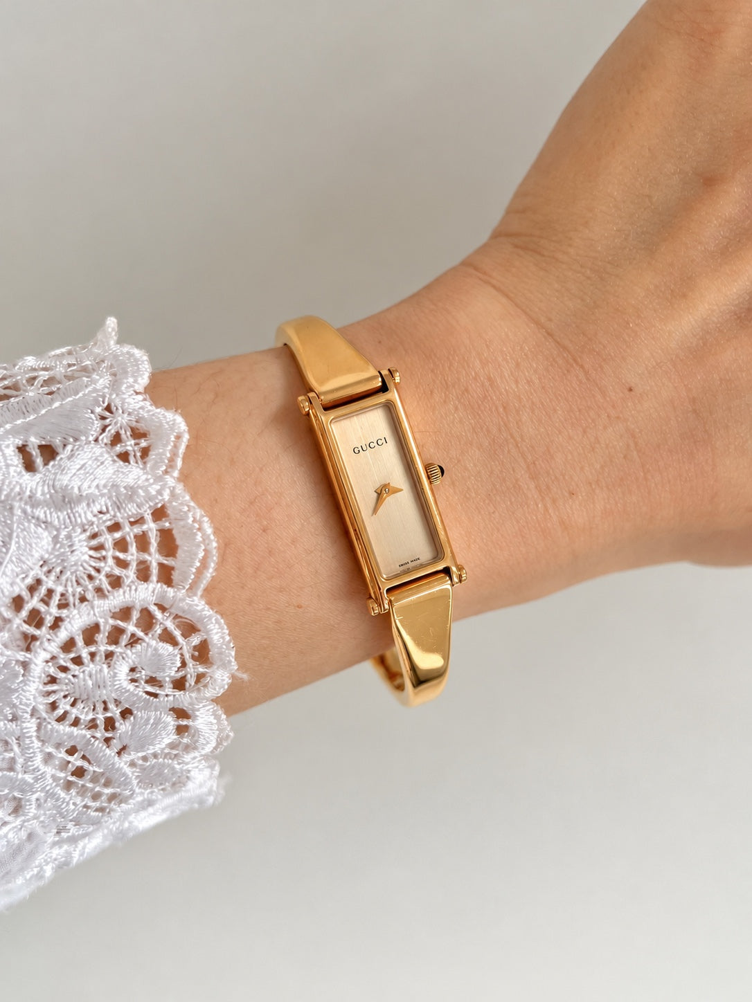 Close view of the Gucci women’s rectangular champagne dial watch, polished rose gold tone bangle and black cabochon crown on the wrist