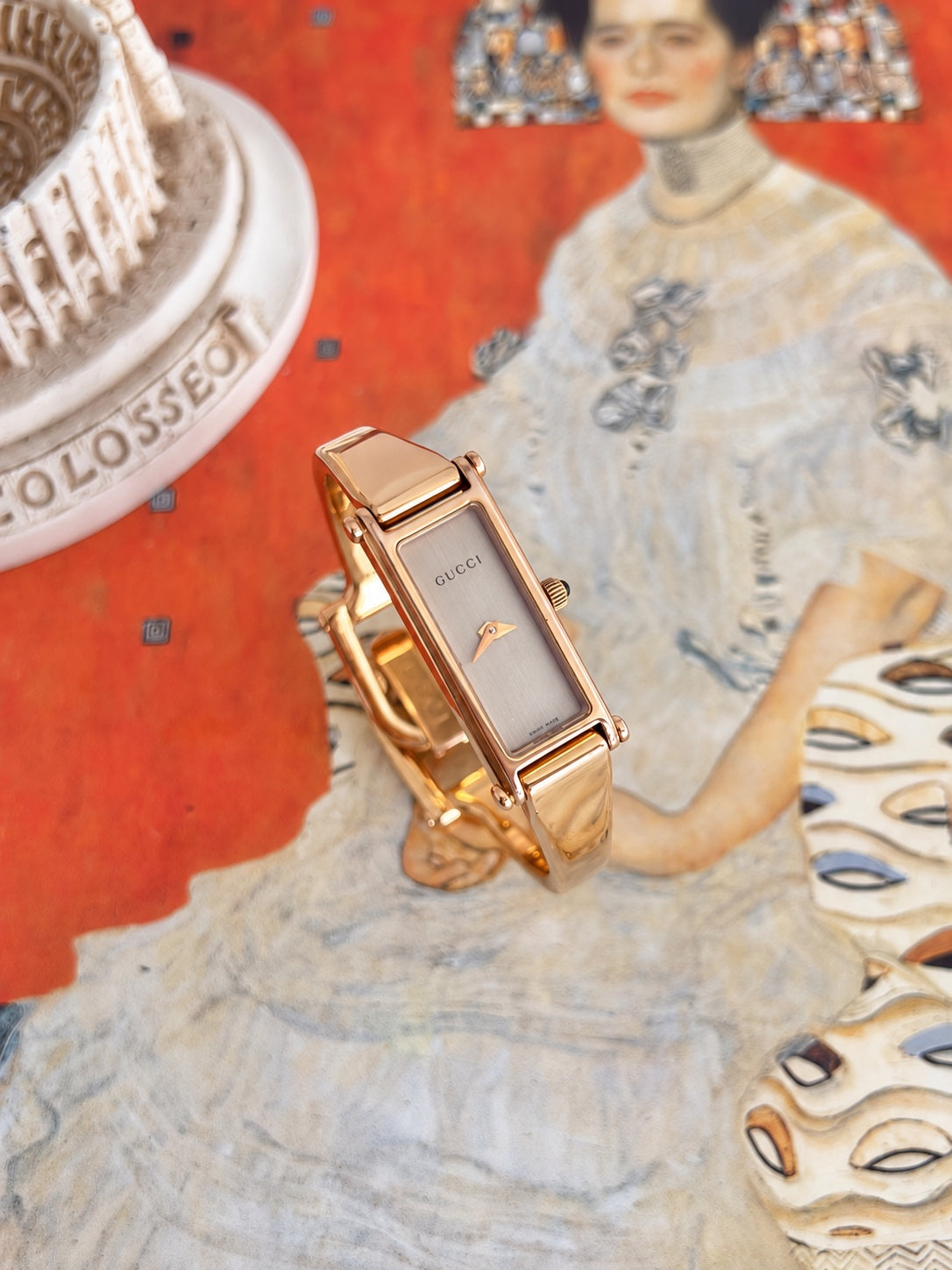 Angled view of the Gucci women’s rose gold tone bangle watch showing its long champagne dial, pin details and black cabochon crown
