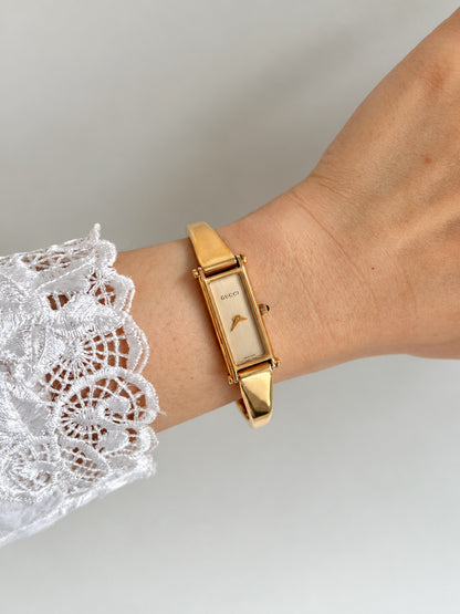 Gucci women’s rose gold tone bangle watch with a narrow champagne dial, worn beside a white lace cuff