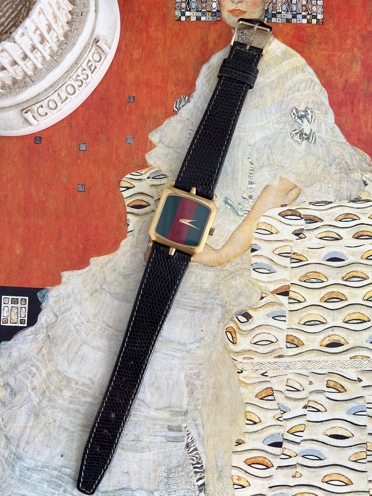 Full view of the Gucci Sherry square gold tone women’s watch with green and red dial, black leather strap and pin buckle.