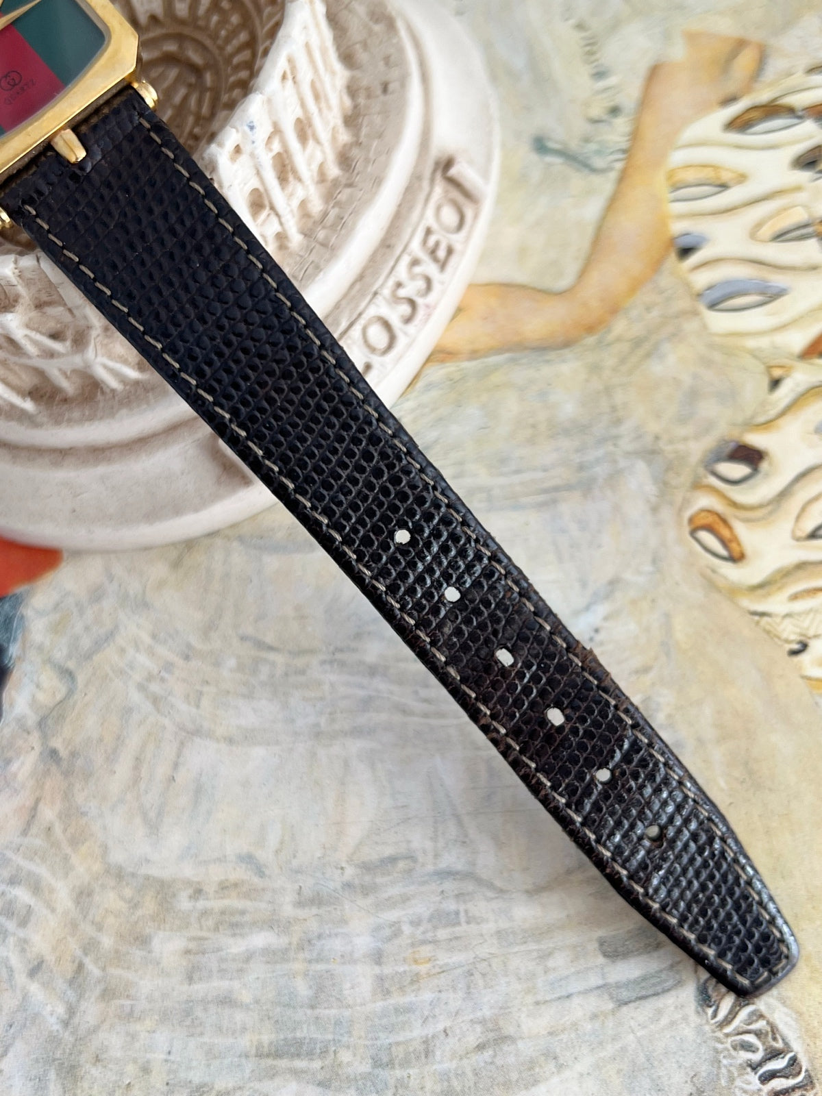 Black textured leather strap and adjustment holes on the Gucci Sherry gold tone women’s watch.