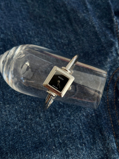 Gucci women’s black dial stainless steel bangle watch shown from the front on blue denim