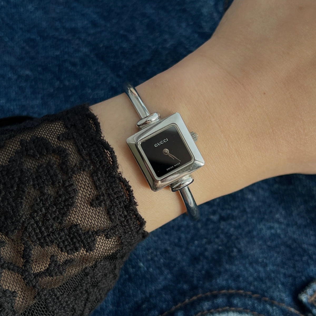 Gucci women’s watch with black square dial and polished stainless steel bangle, worn with a black lace sleeve