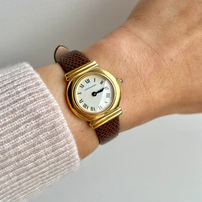 Hamilton Roman dial women’s watch worn on wrist with gold round case and brown textured strap