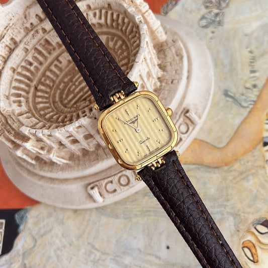 Longines gold tone cushion women’s watch showing circular dial details and polished dot hour markers beside a Colosseum model.