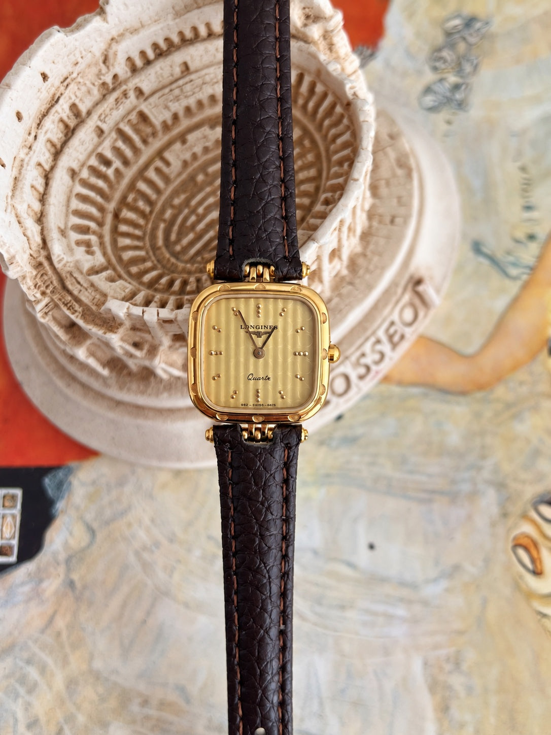 Front view of the Longines champagne patterned dial watch with paired dot markers, gold tone cushion case and brown leather strap.