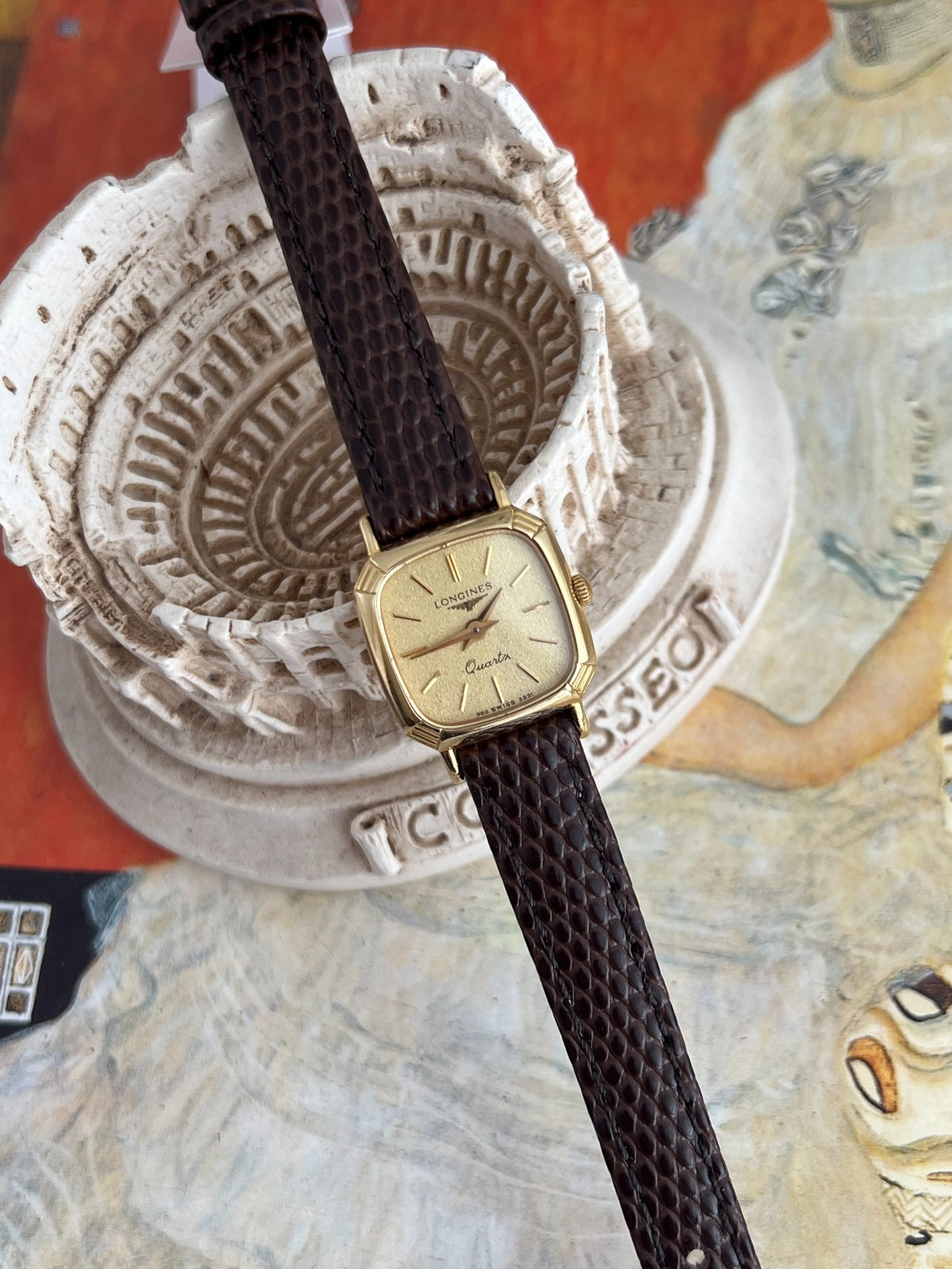 Longines gold tone cushion watch and brown patterned Hirsch leather strap in a full still life view.