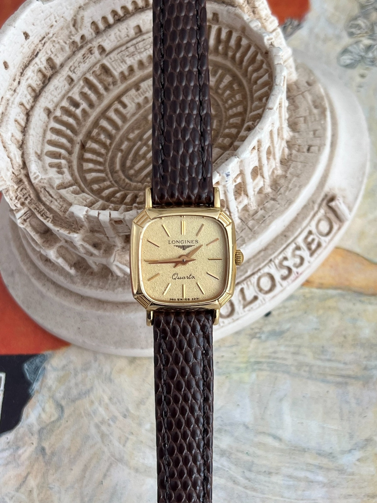 Front view of the Longines champagne dial watch with grooved gold tone cushion case and brown Hirsch leather strap.