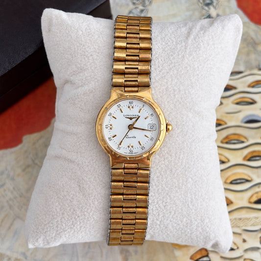 Longines Conquest white dial with gold baton markers, paired dot accents, three hands and date at three, in a gold tone case.