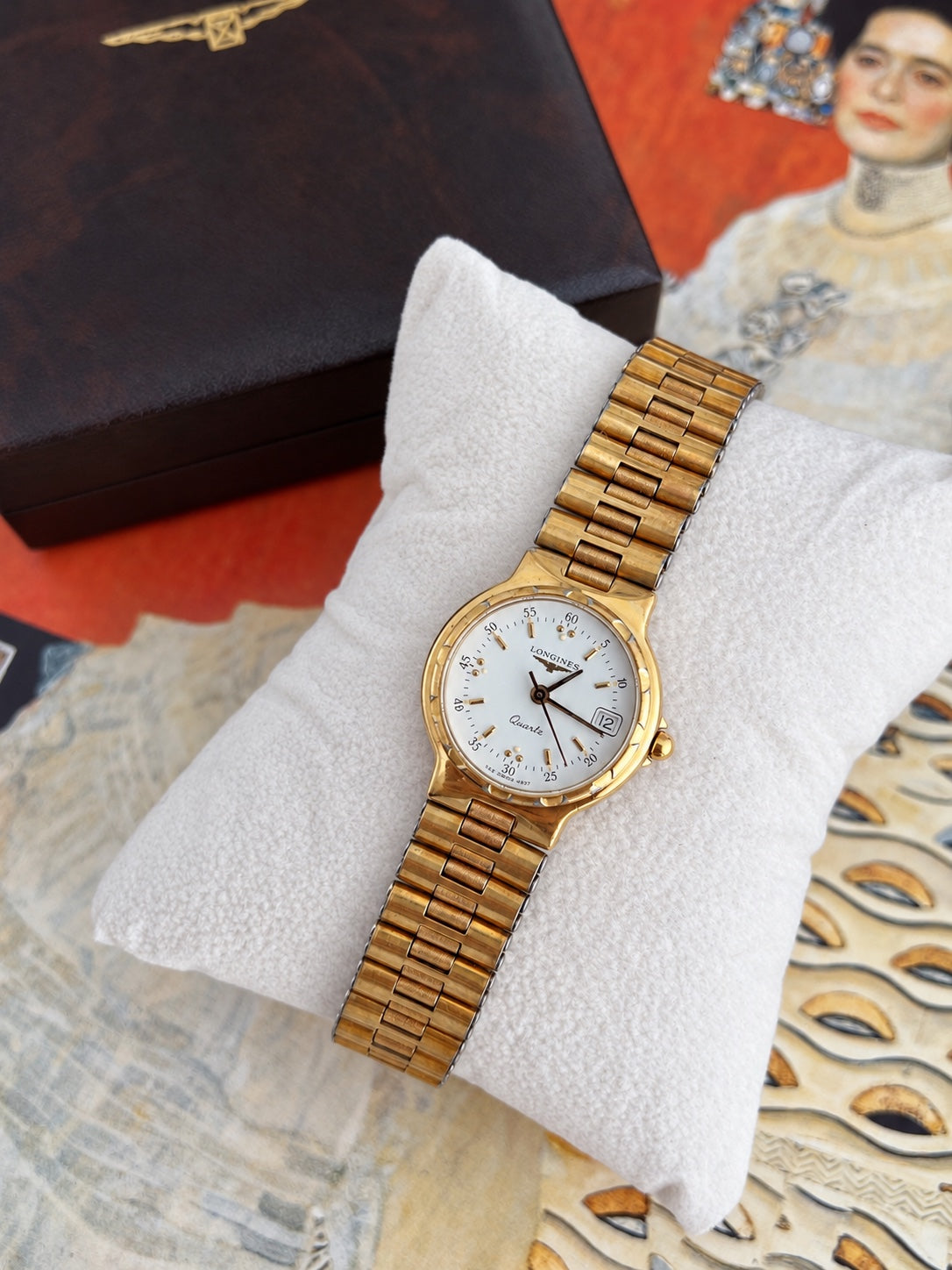 Full view of the Longines Conquest gold tone bracelet watch with white dial and date window, on a display cushion.