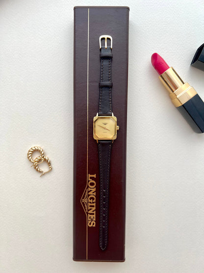 Longines square gold-tone ladies watch with black strap shown on the wrist.