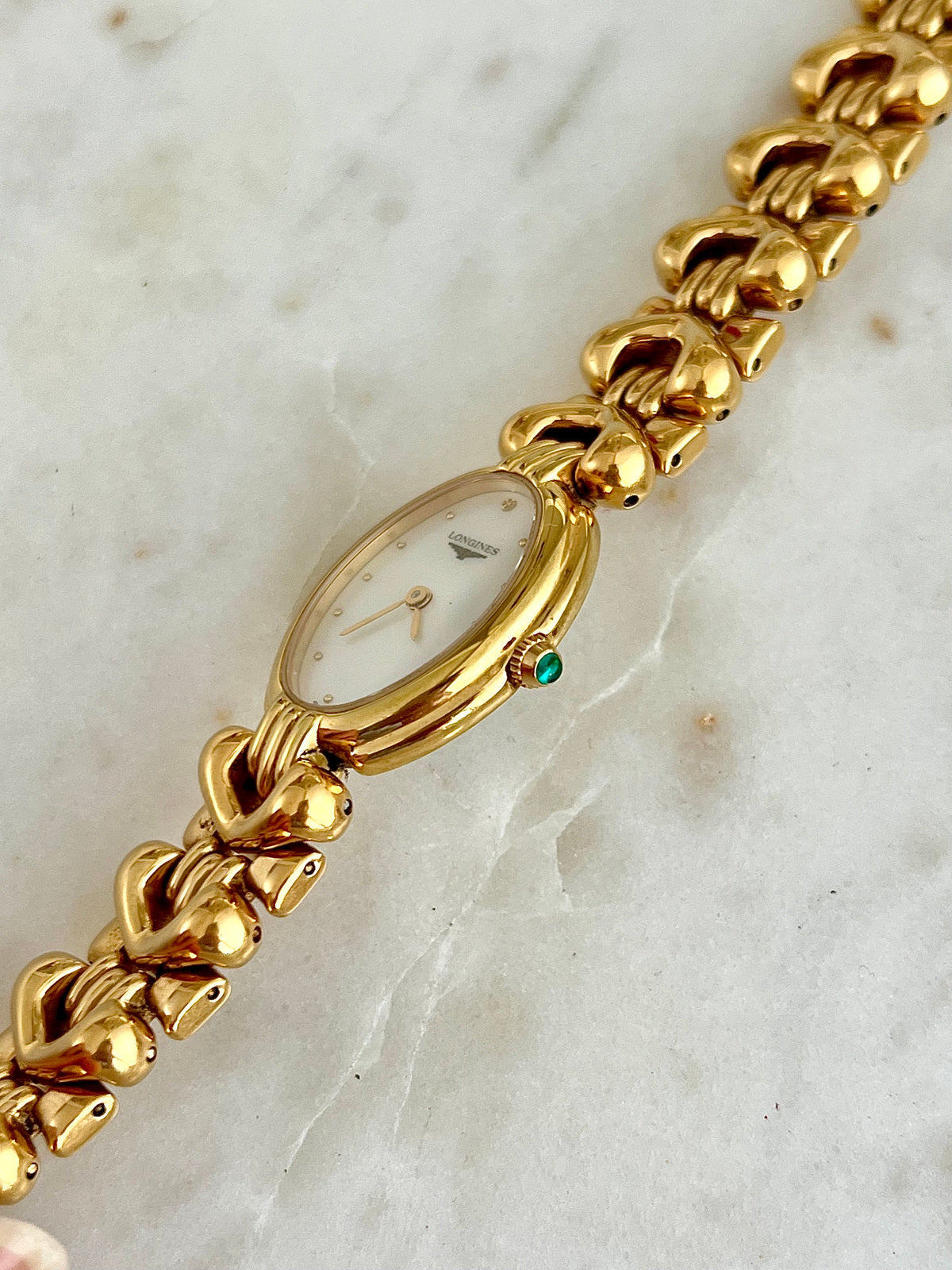 Close angled detail of the Longines Equestrian L6.132.2 gold-tone horseshoe bracelet watch and pale dial
