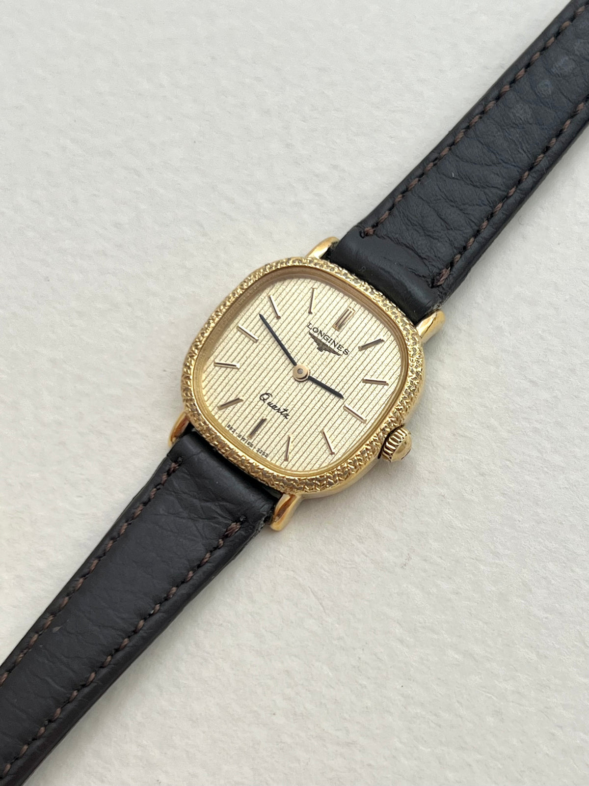 Front view of the Longines gold cushion ladies watch with striped champagne dial and engraved bezel.