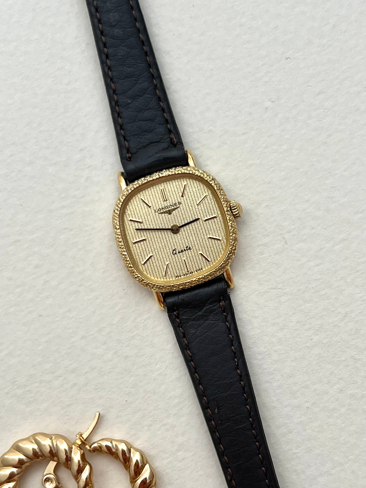 Longines gold cushion ladies watch with striped champagne dial shown on the wrist.