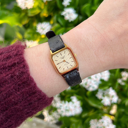 Longines gold faceted women’s watch with fluted champagne dial and black leather strap worn on wrist