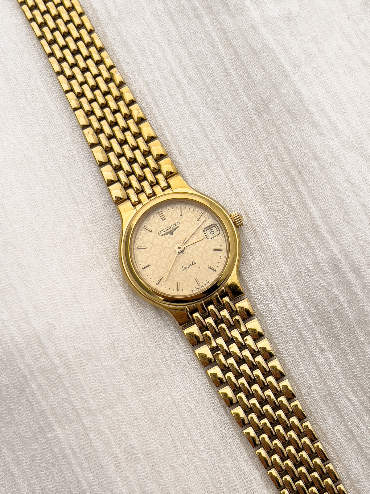 Vintage Longines ladies watch with gold-tone round case and patterned dial.