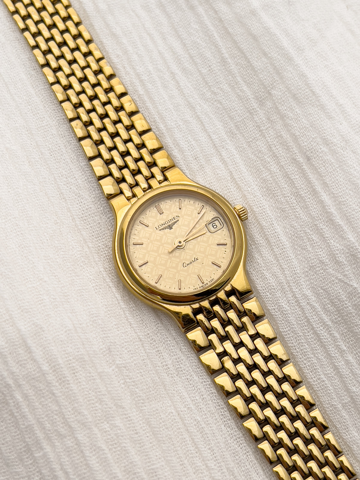 Gold-tone Longines women's quartz watch with patterned dial and date window.