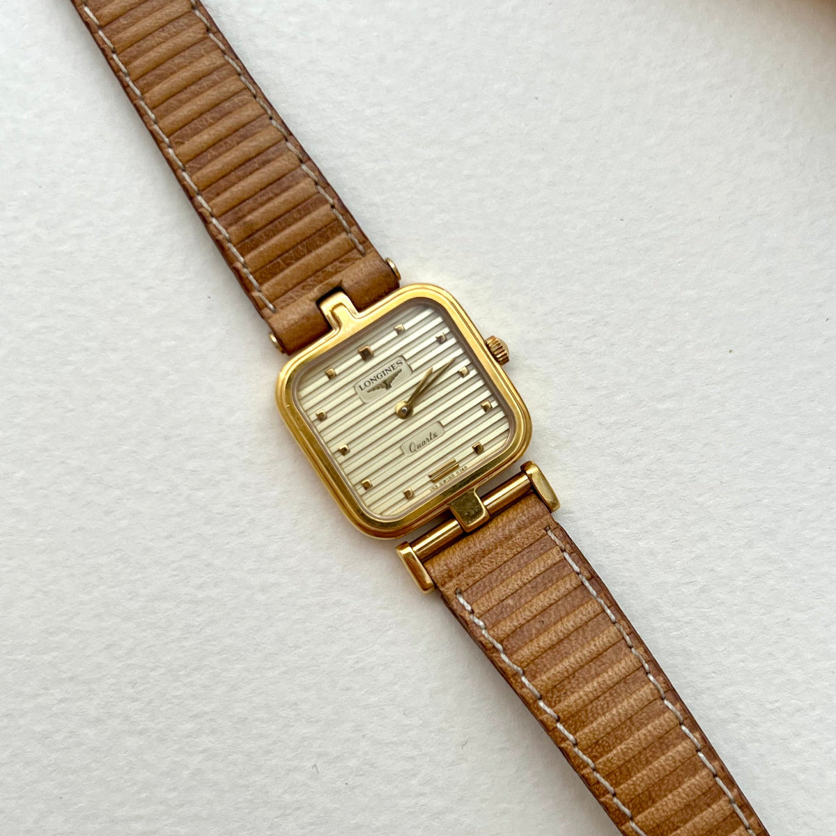 Longines gold square-cushion watch with honey-tan leather strap shown on a white background.