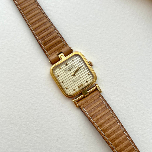 Longines gold square-cushion watch with honey-tan leather strap shown on a white background.