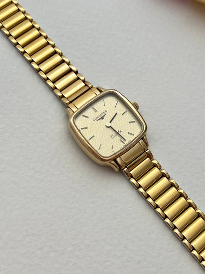 Close-up detail of the Longines gold-tone brick-style integrated bracelet and embossed clasp.
