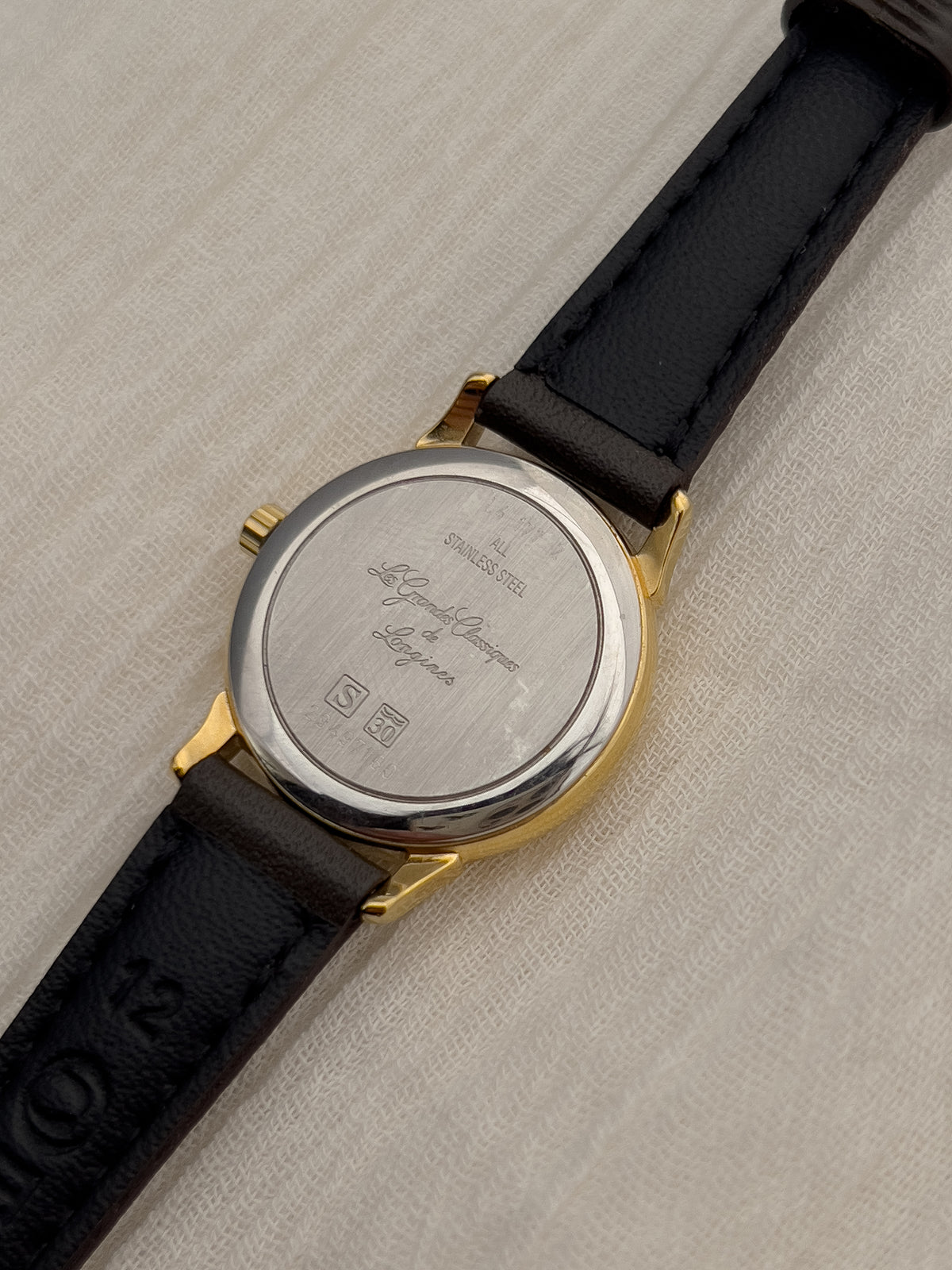 Wrist view of the Longines gold ladies watch with champagne dial and brown strap.