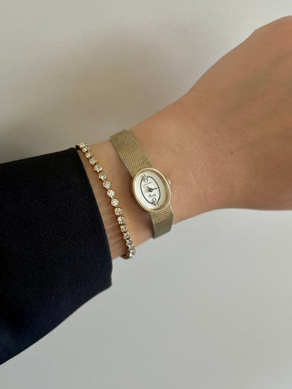 Wrist view of the Longines oval crystal-accent watch with woven gold bracelet.
