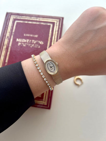 Angled detail of the Longines gold-plated oval case and fluid Milanese bracelet.